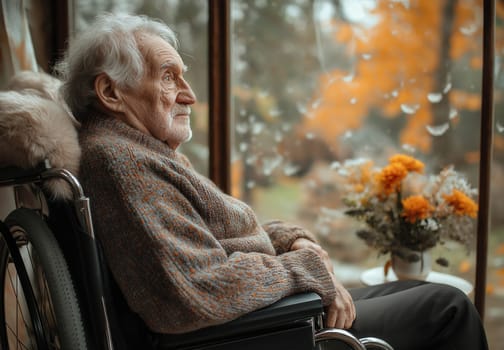 An elderly man sits in a wheelchair looking into the distance. Selective focus.