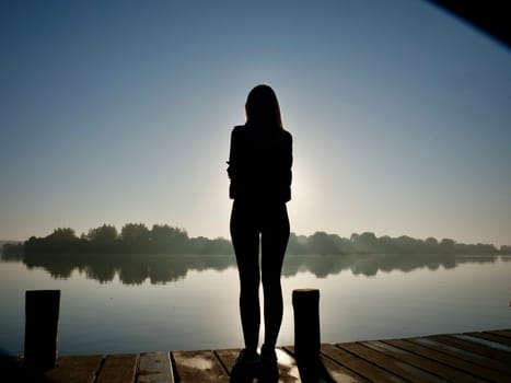 Woman standing on sadhu board, process of standing barefoot on nails, view of feet practicing yoga and meditation outdoors, autumn day near lake at sunrise