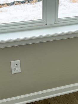 Castle Pines, Colorado USA - January 18, 2023-Close-up of a clean wall outlet beneath a large window with a white window ledge in a newly constructed single-family home. The neutral-colored walls and baseboard highlight the modern design and attention to detail in the home.