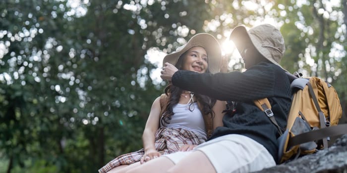 Two women, a loving couple, sitting closely on a rock, smiling at each other as they enjoy their hiking adventure in a beautiful, sun drenched natural setting.