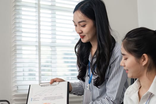 A professional woman explains a report chart to her teammate, highlighting teamwork and effective data analysis in a bright office environment.