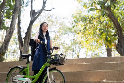 A friendly businesswoman stands beside her sustainable bicycle on steps in a sunny park, promoting energy saving transportation and an eco conscious lifestyle.