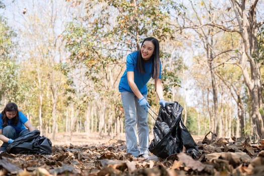 A young woman in a blue shirt joyfully collecting trash in a forest, showcasing her commitment to community service and environmental care.