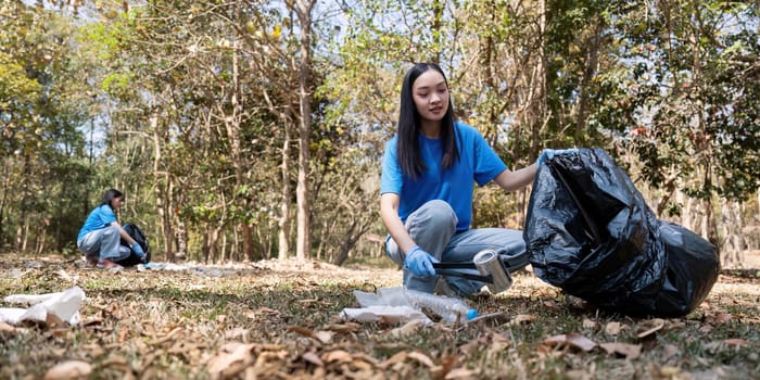 A young woman in a blue shirt carefully picking up litter in a forest, highlighting her commitment to environmental responsibility and community service.