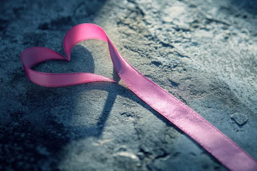 This minimalistic image features a pink ribbon shaped like a heart, resting gently on a textured surface. The soft, delicate design symbolizes love and affection, creating an artistic and serene atmosphere.