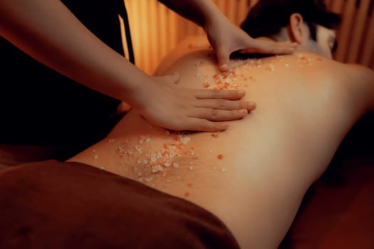 Man customer having exfoliation treatment in luxury spa salon with warmth candle light ambient. Salt scrub beauty treatment in Health spa body scrub. Quiescent