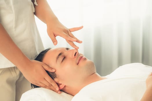 Caucasian man enjoying relaxing anti-stress head massage and pampering facial beauty skin recreation leisure in dayspa modern light ambient at luxury resort or hotel spa salon. Quiescent