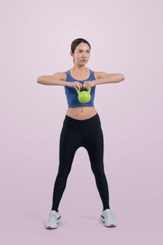 Vigorous energetic woman doing kettlebell weight lifting exercise on isolated background. Young athletic asian woman strength and endurance training session as body workout routine.