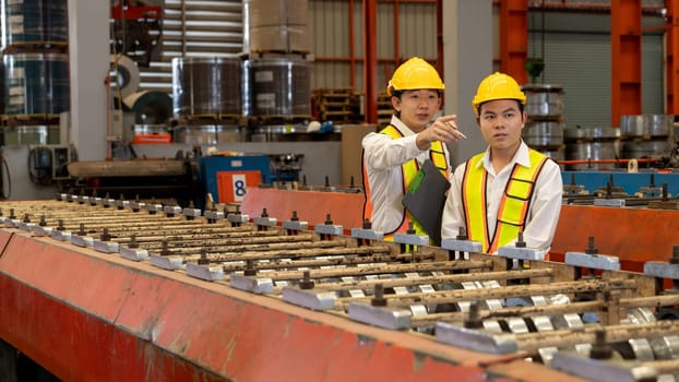 Factory worker operating metal stamping machine while supervised by engineer for optimal quality output of industrial goods on assembly steel forming line in heavy industry factory. Exemplifying