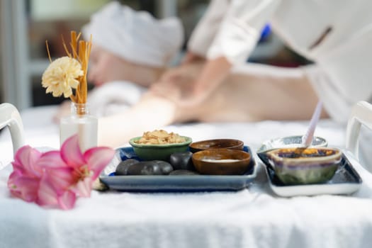 Natural herbal ingredient of facial mask and floral essence was placed on white towel in front of beautiful woman having body massage by professional masseuse. Blurring background. Tranquility.