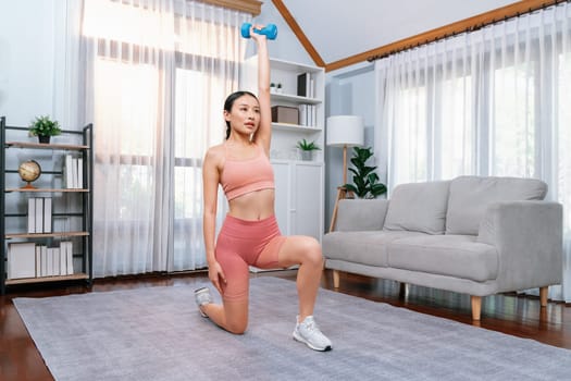 Vigorous energetic woman doing yoga with dumbbell weight lifting exercise at home. Young athletic asian woman strength and endurance training session as home workout routine.