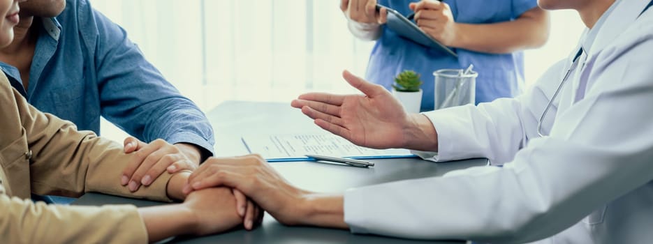 Doctor providing compassionate healthcare consultation while young couple patient holding hand, comfort each other after infertile report. Reproductive and medical fertility consulting. Neoteric