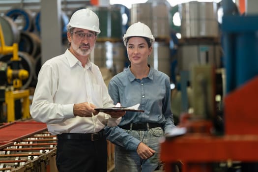 Factory engineer manager with assistant using laptop to conduct inspection of steel industrial machine, exemplifying leadership as machinery engineering inspection supervisor in metalwork manufacture.