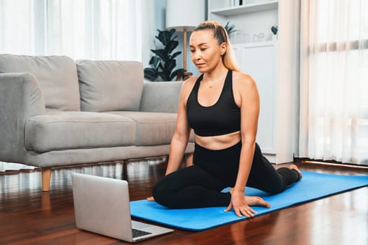 Senior woman in sportswear being doing yoga in meditation posture on exercising mat at home. Healthy senior pensioner lifestyle with peaceful mind and serenity. Clout