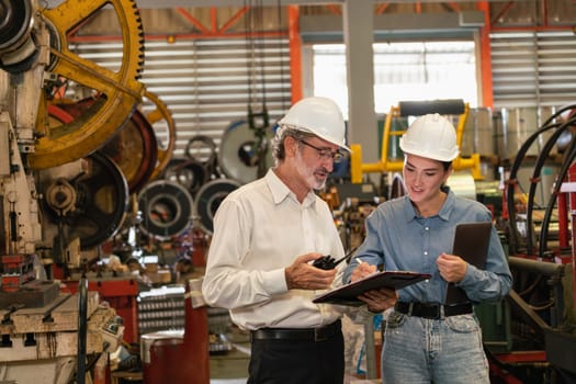 Factory engineer manager with assistant using laptop to conduct inspection of steel industrial machine, exemplifying leadership as machinery engineering inspection supervisor in metalwork manufacture.