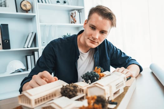 Architect designer studies elegant house model, reviewing structure design for improvement with construction plan on table. Creativity and innovation in architectural design. Iteration