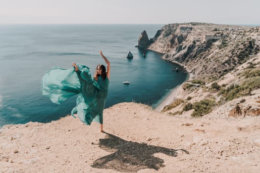 Woman green dress sea. Female dancer posing on a rocky outcrop high above the sea. Girl on the nature on blue sky background. Fashion photo