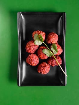 meatballs with parsley on a black plate, on a green background. View from above. Chinese cuisine, ingredient for hotpot