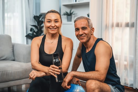 Athletic and sporty senior couple portrait in sportswear sitting on sofa with fitness water bottle as home exercise concept. Healthy fit body lifestyle after retirement. Clout