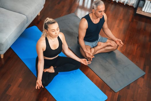 Happy active senior couple in sportswear being doing yoga in meditation posture on exercising mat at home. Healthy senior pensioner lifestyle with peaceful mind and serenity. Clout