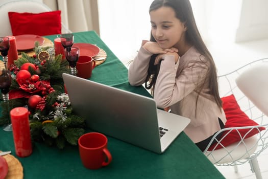 Cute girl using computer by christmas tree.