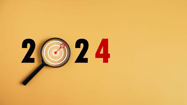 The dartboard icon in a magnifying glass centered on the number 2024 on a yellow background. Represents the goal setting for 2024, the concept of a start. financial planning development strategy business goal setting