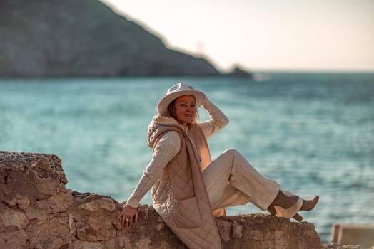 Happy blonde woman in a white suit and hat posing at the camera against the backdrop of the sea.