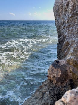 Seascape with a view of the rocky coast, beautiful sea surface, waves crashing on a rocky cliff. A clear sunny day.