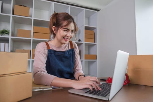 Happy young Asian woman entrepreneur, Smile for sales success after checking order from online shopping store in laptop at home office, Concept of merchant business online and eCommerce.