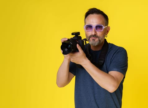 Stylish and creative mid-aged photographer with mirrorless camera against yellow background. Purple glasses adding touch of flair, modern and artistic photographer who involved both style and creativity. High quality photo