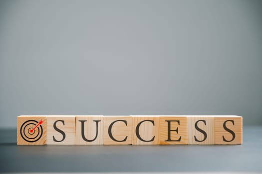 Symbolic representation of target success with a wooden cube positioned over the word success on a wood table. Captured on a minimalistic grey background.