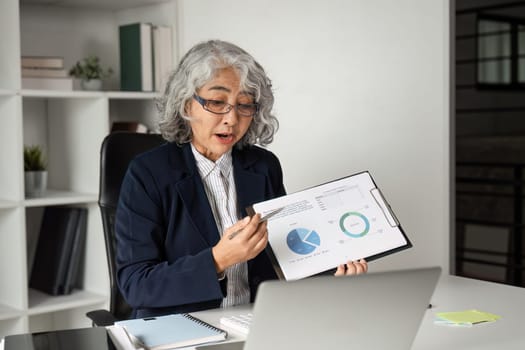 Experienced businesswoman presenting data via online meeting, showcasing graphs and charts in a professional office environment.