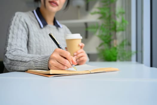 Close up of young woman writing in notebook while sitting in a bright, natural light filled space.