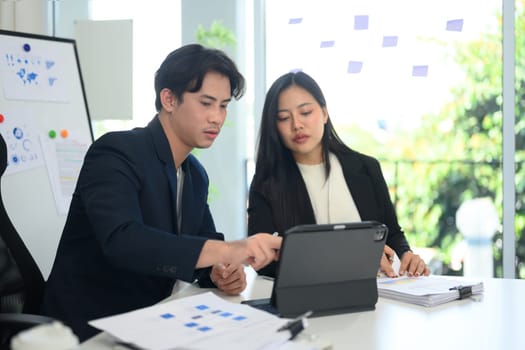 Two businesspeople analyzing data displayed on digital tablet at bright office.