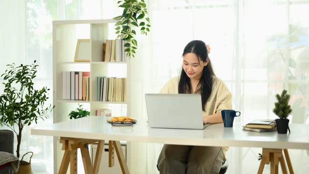Focused young asian woman working in a bright home office.
