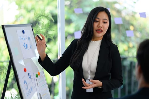 Confident businesswoman in a black suit presenting data on whiteboard during meeting.