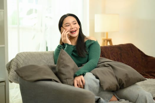 Attractive young woman in a green sweater enjoying a phone conversation at home.