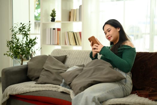 Relaxed young woman in sweater and jeans using smartphone on a cozy sofa.