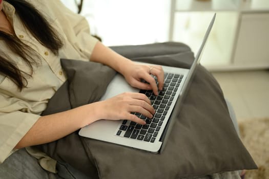 Close up of female freelancer working on a laptop placed on cushion.
