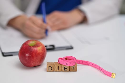 A nutritionist writing notes on healthy diet choices with an apple and measuring tape to guide others