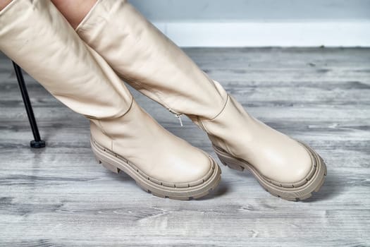 A model poses gracefully indoors, showcasing stylish beige knee-high boots that highlight contemporary fashion trends.