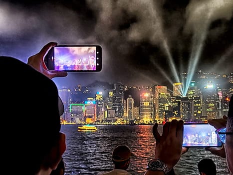 Hong Kong - April 05, 2024: Visitors enjoy a breathtaking evening light show at Victoria Harbour, capturing the vibrant skyline of Hong Kong. The colorful display enhances the iconic cityscape as night falls.