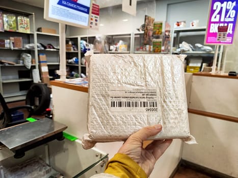 Kirov, Russia - October 06, 2024: A person holds a package from China at a post office in Russia while surrounded by various postal items and signage.