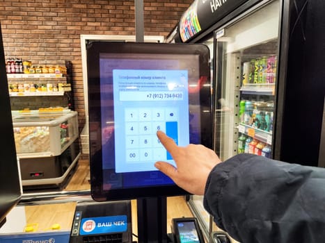 Kirov, Russia - December 03, 2024: Customer interacts with a touchscreen to weigh items and input payment details at a self-service checkout station in a grocery store.