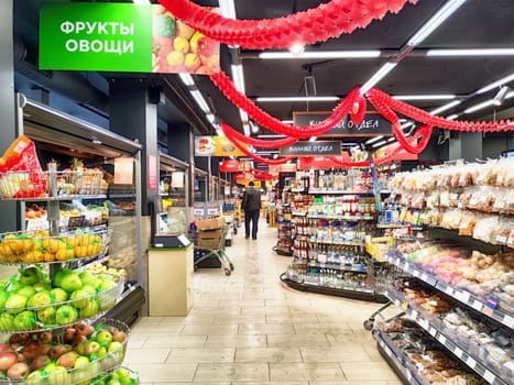 Kirov, Russia - December 11, 2024: Brightly lit grocery store features a self-service checkout area and well-arranged displays of fresh fruits and snacks in the aisles.