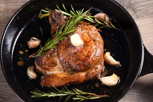 Pork cutlet on the bone in a piece of butter with garlic and rosemary in a frying pan 
