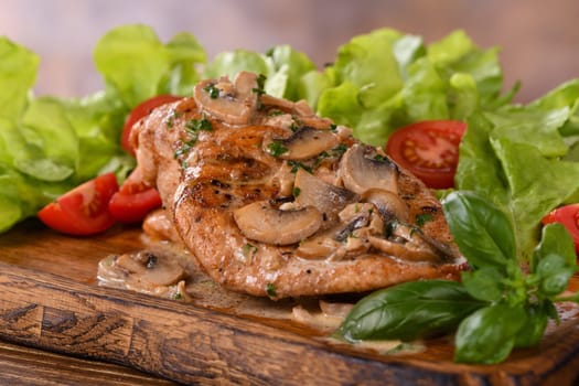 Chicken breast with mushroom sauce and vegetables on a wooden plate