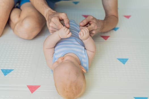A baby lies on a soft children play mat while their father hands gently support and protect them. Heartwarming moment of care and connection. Parenthood, safety, and love concept.
