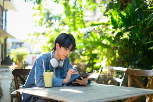 Stylish young man wearing a denim jacket using digital tablet at an outdoor cafe.
