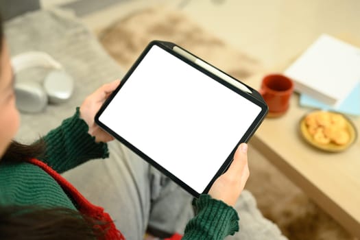 Close up of a woman holding a tablet with a blank white screen, while sitting comfortably at home.